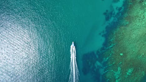 Birdseye-view-boat-cruising-alongside-coral-reef,-Yasawa-islands,-FIji