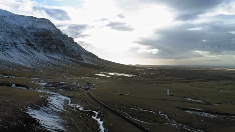 volando sobre el hermoso paisaje marrón junto a la montaña rocosa nevada, islandia - antena
