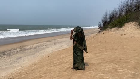 An-Indian-woman-in-green-saree-standing-near-a-yellow-beach-at-Konark-Sun-Temple,-Orissa