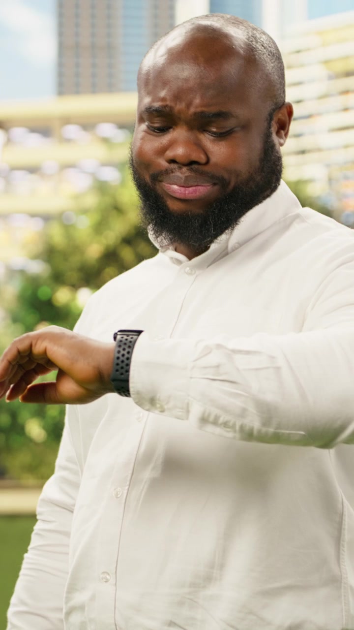Vertical Video Concerned businessman checking time on smartwatch while standing in city park
