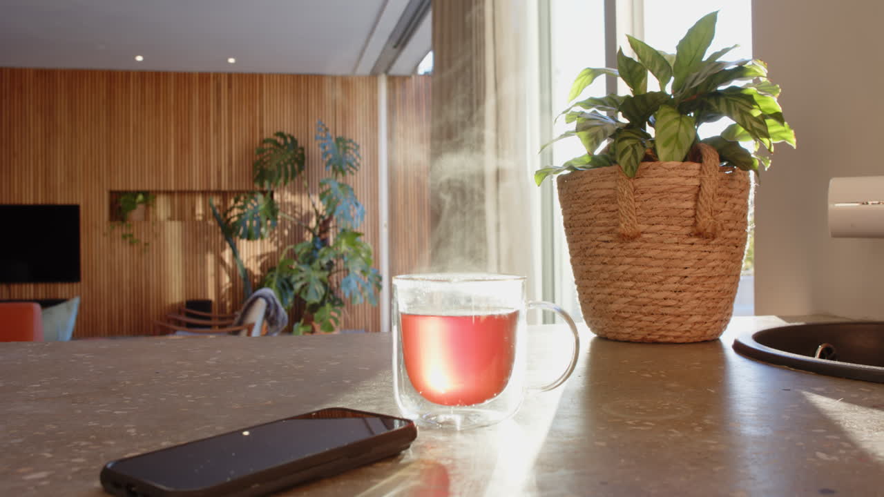 Steaming cup of tea on kitchen counter with smartphone and potted plant, copy space