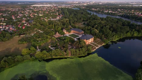 Mogoșoaia-palace-in-romania,-lush-greenery-and-reflective-lake-at-sunset,-aerial-view