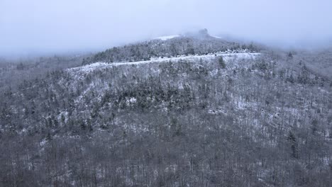 Flying-through-clouds-and-towards-snow-covered-mountains-and-forests-in-a-beautiful-mountain-valley-during-winter-on-a-cloudy-day