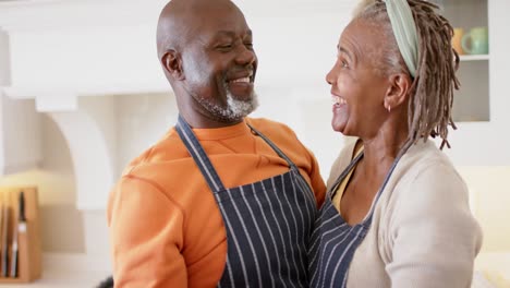 Happy-african-american-senior-couple-in-aprons-dancing-in-kitchen,-slow-motion