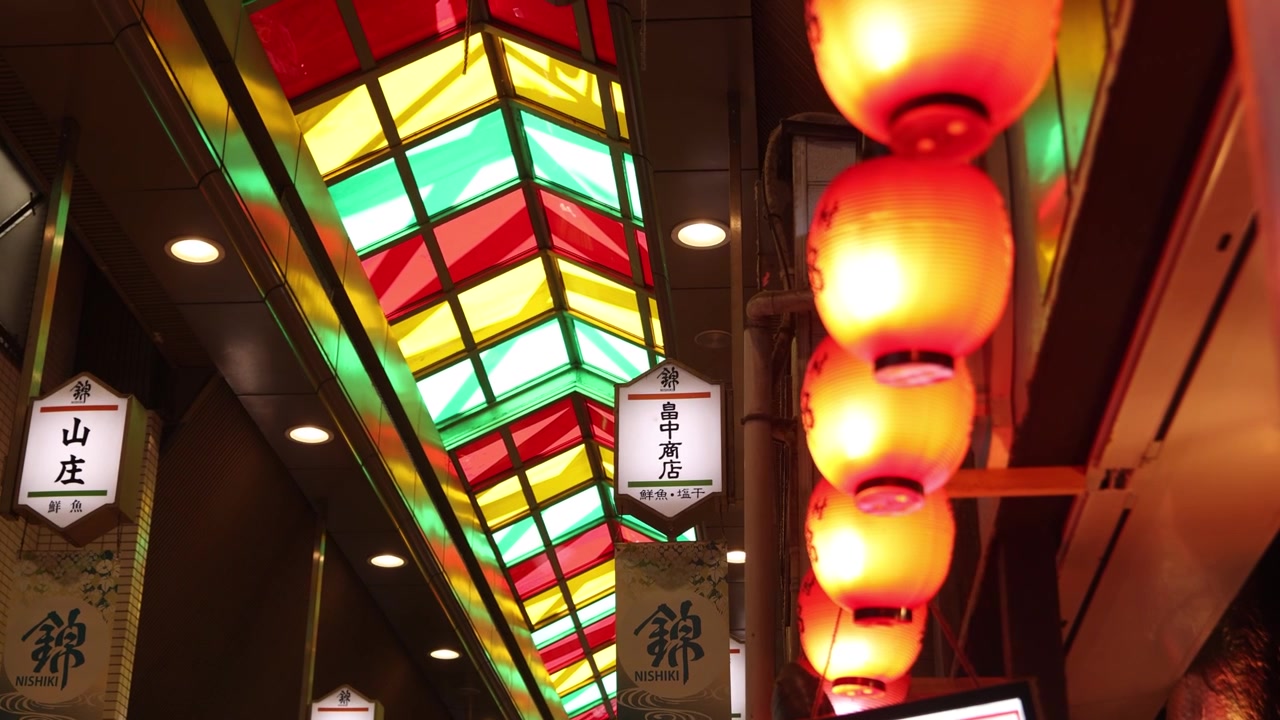 Udsigt inde fra Nishiki-markedet i Kyoto, Japan, med dets karakteristiske farverige overdækkede arkade, traditionelle butikker og atmosfæriske lanterner langs den berømte historiske handelsgade