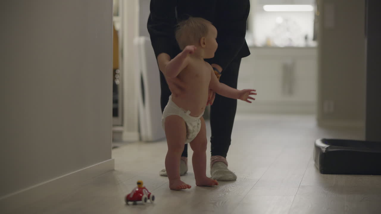 Baby in a diaper learning to walk with support indoors, a milestone moment of growth