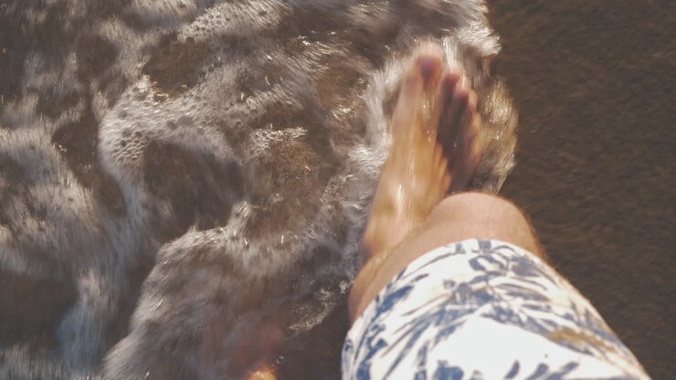 Turista che cammina lungo la costa del mare con le onde che gli lavano i piedi.