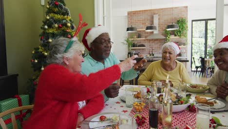 Verschiedene-ältere-Freunde-Mit-Weihnachtsmützen-Schauen-Auf-Ihr-Smartphone-Und-Lachen-Am-Weihnachtstisch