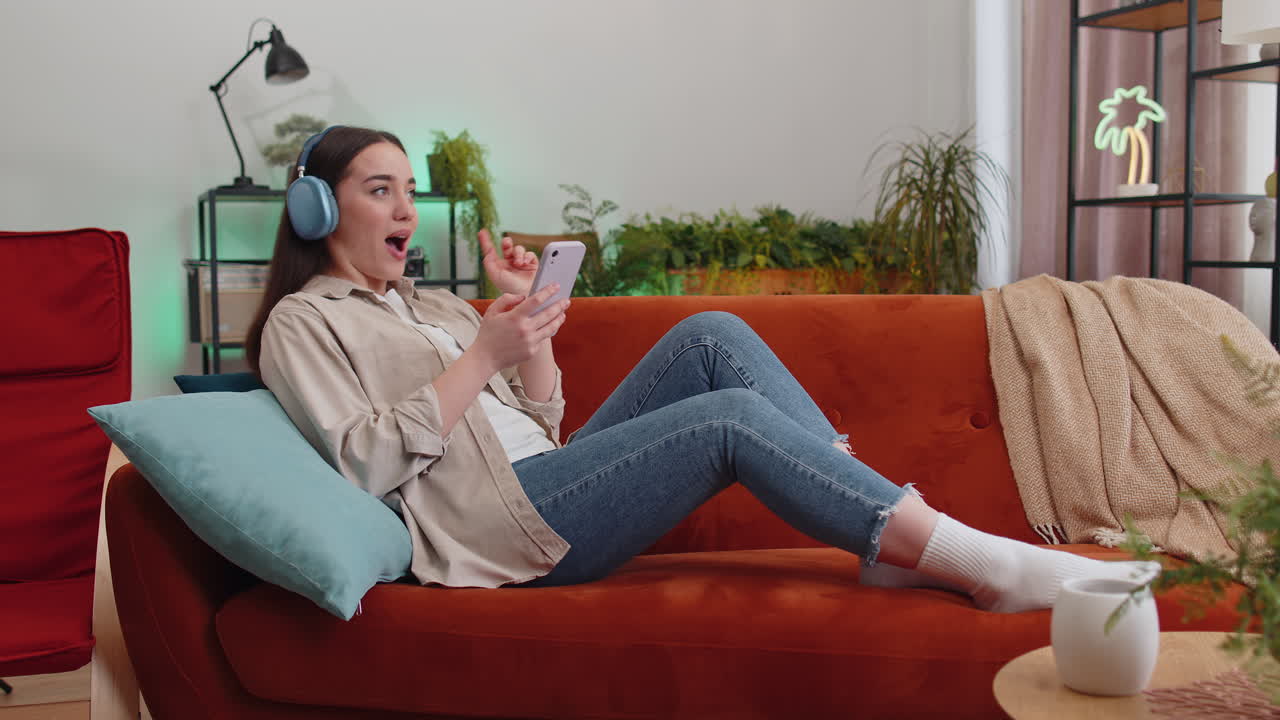 mujer joven feliz con auriculares inalámbricos relajándose acostada en el sofá en casa escuchando su música favorita