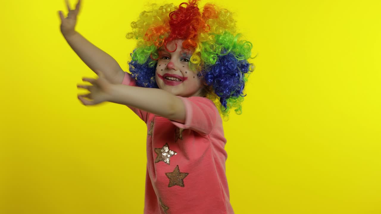 niña pequeña payaso con peluca colorida haciendo caras tontas, gritando, agarrando la cabeza, agitando las manos