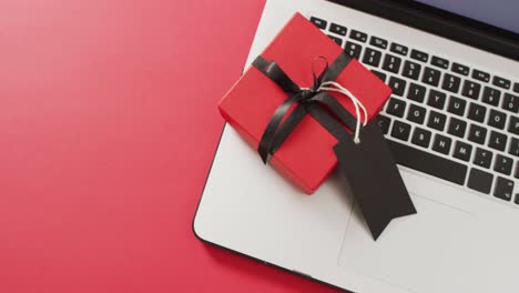 portátil y caja de regalo roja con cinta negra y etiqueta de regalo, sobre fondo rojo con espacio para copiar