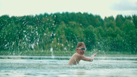 a joyful caucasian kid splashes the water with hands and having fun in the lake