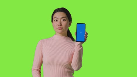 Studioporträt-Einer-Frau,-Die-Ein-Bluescreen-Handy-In-Richtung-Kamera-Vor-Einem-Greenscreen-Hält