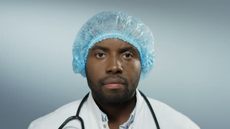 close up of the young handsome man doctor looking straight to the camera with a serious face on the grey wall background