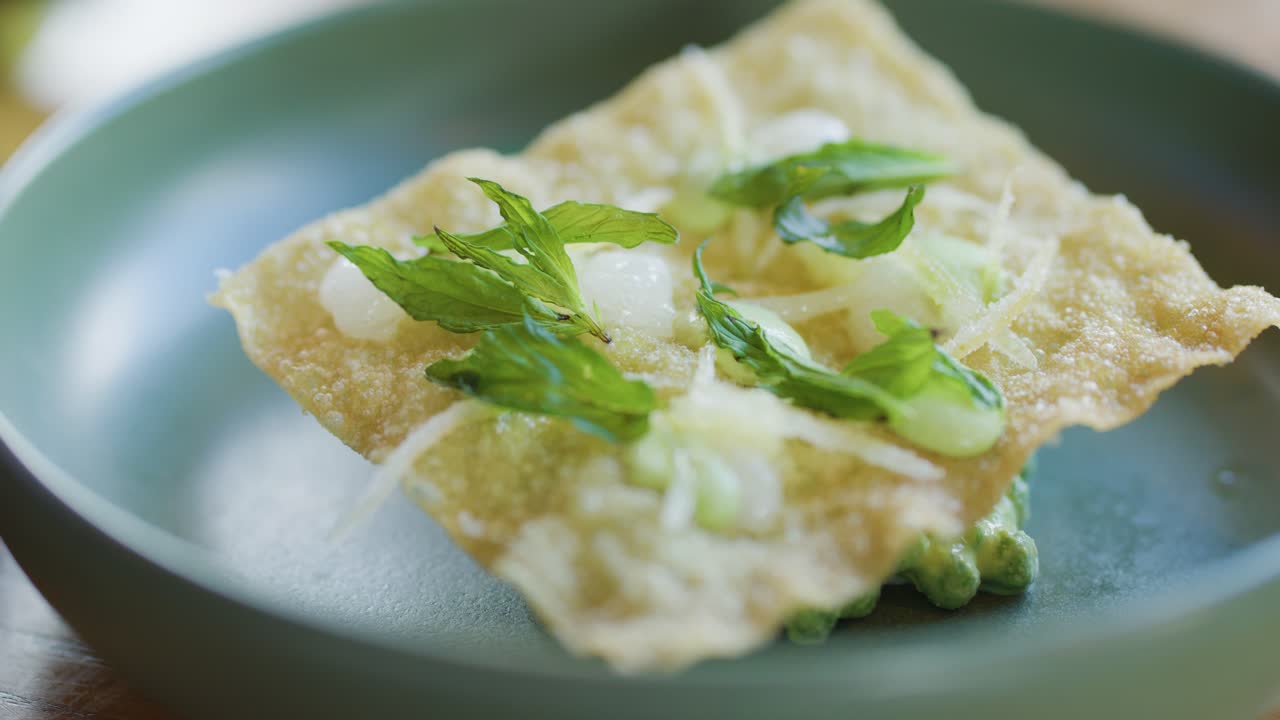 A fork and knife slice through a crisp seafood crab cake topped with fresh greens on a green plate, under soft natural lighting, macro perspective
