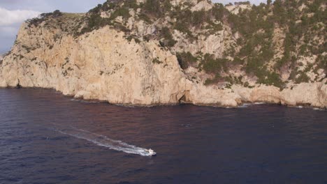 small fishing boat cruising at ocean at high cliffs of cap formentor mallorca,aerial