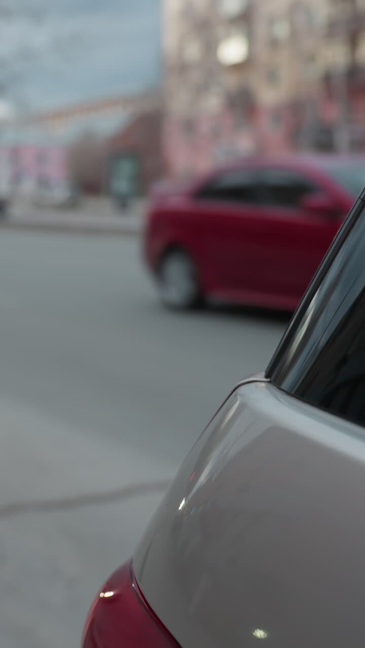 Close-up view of a parked car with a red car approaching from behind and another car with headlights visible in the distance