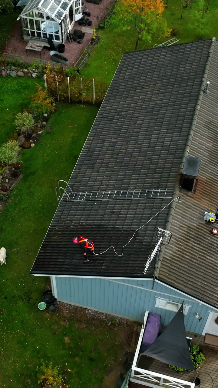 Aerial portrait rising in front of a worker power washing a dirty house roof