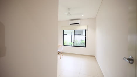 small bedroom or office space staged with white wooden desk and minimalistic shelf, window open to tropical outside