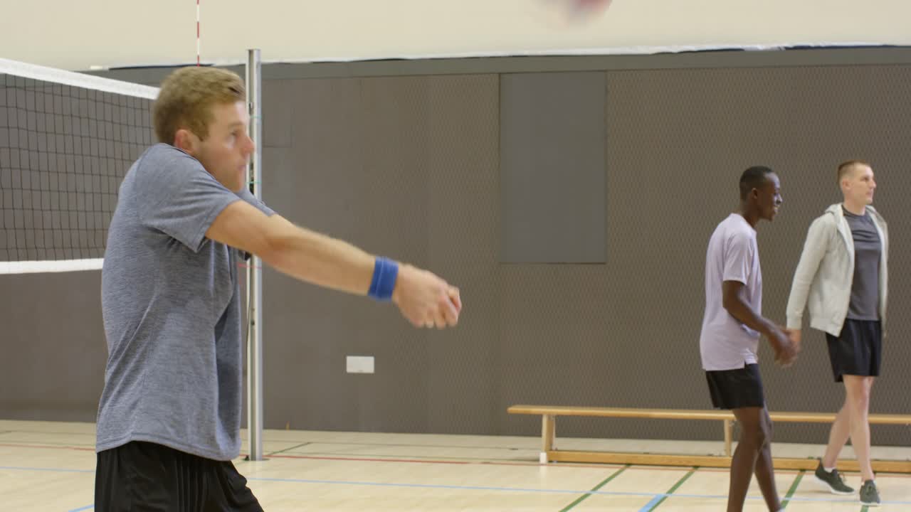 Diverse male team drilling in gym, ball entering from right, center bumping volleyball, copy space