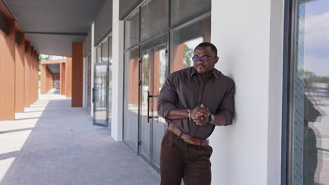 zoom out view of the happy handsome man standing by the modern office and checking time while waiting somebody. pleasant mood because of good day. successful start up and positive emotions concept