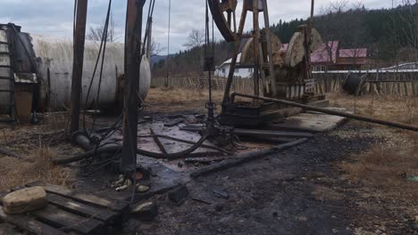 equipo de perforación petrolera con tanque de almacenamiento en un campo con edificios y montañas en el fondo