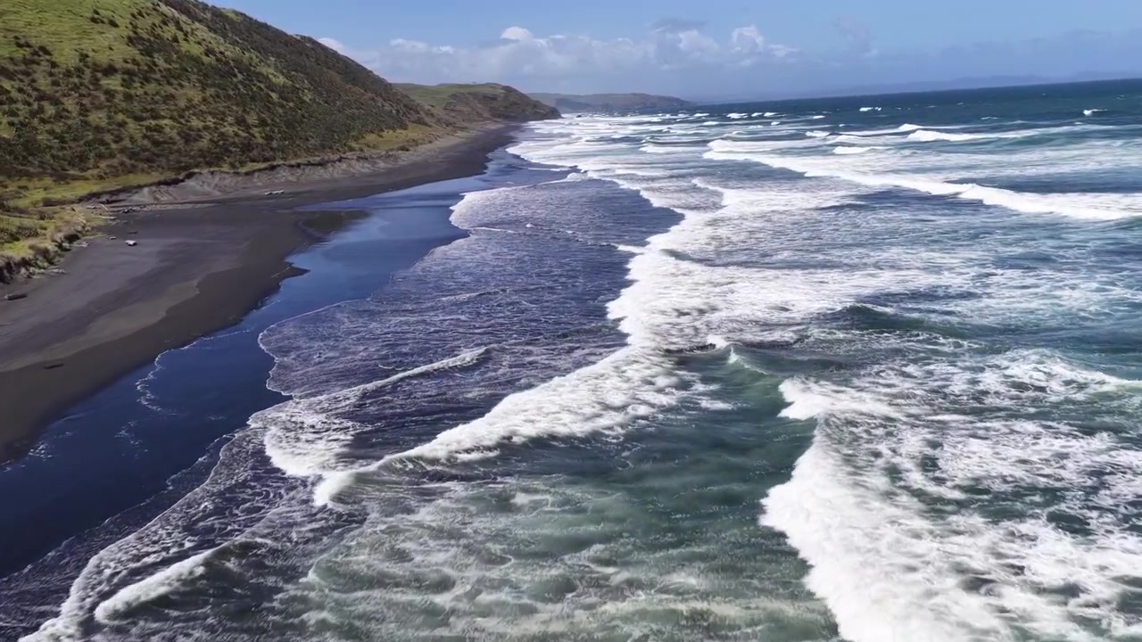 Onde dell'oceano si infrangono lungo una costa di sabbia nera sull'Isola del Nord della Nuova Zelanda