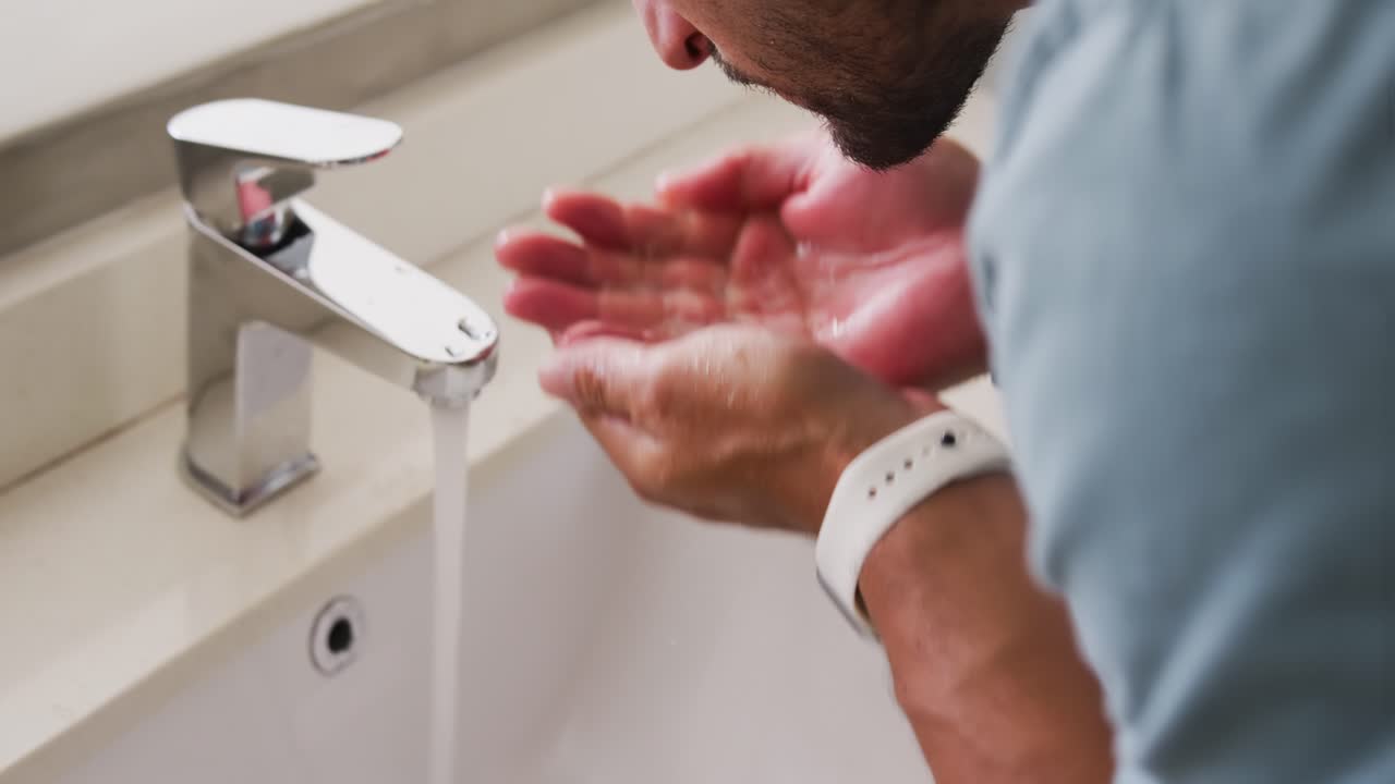 Adult man reacting to running faucet, cupping water, splashing and rinsing face at sink, copy space
