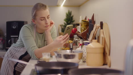 woman works in the kitchen and browses the internet on her smartphone