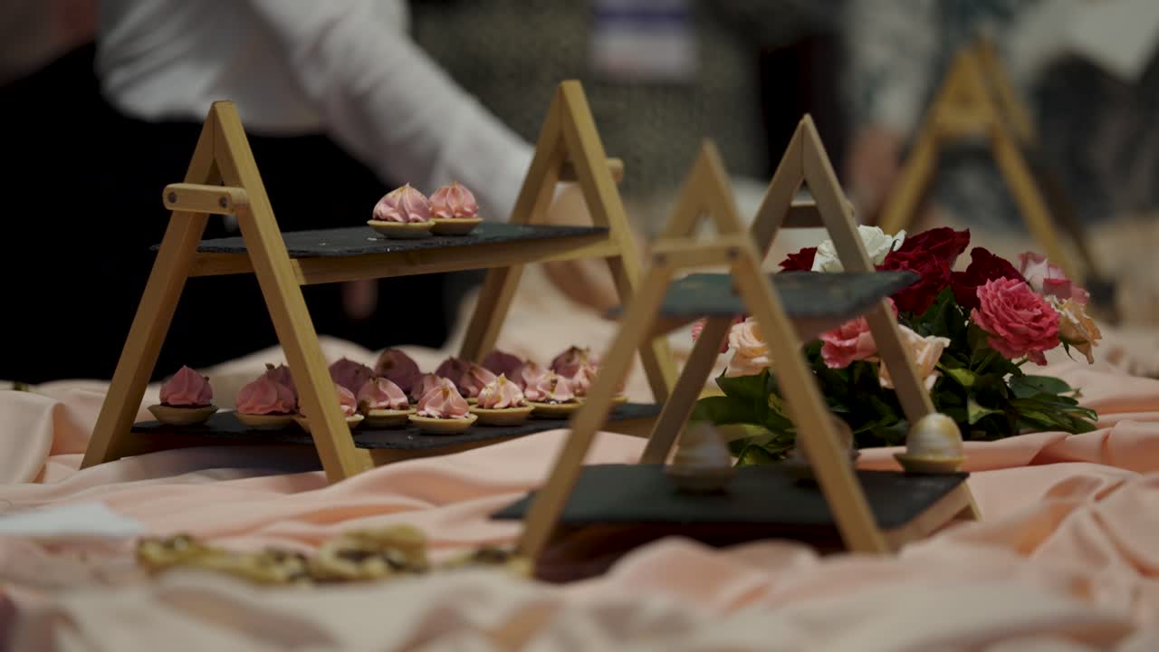A beautiful display of delicate pink pastries on modern, tiered serving stands made of wood and slate. This elegant dessert table is ready for guests at a wedding, gala, or corporate event