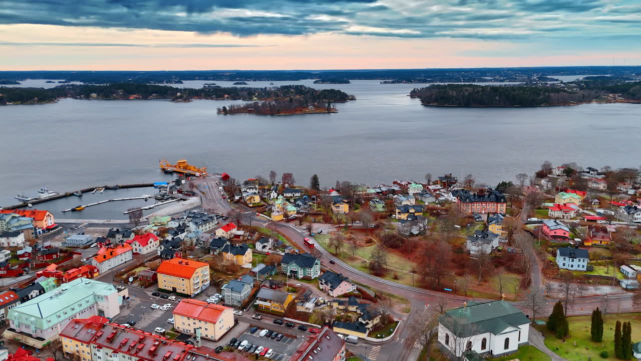 Vista aérea del frente marítimo de Vaxholm con iglesia y ferry. Toma de ángulo alto de un puerto de ciudad costera con un ferry amarillo, iglesia y casas residenciales coloridas.