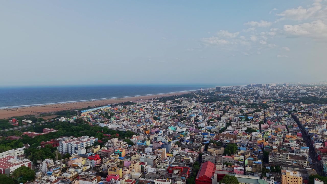 Ripresa aerea con drone che mostra la densa e colorata città di Chennai che si estende verso Marina Beach e il Golfo del Bengala con edifici residenziali, vegetazione e paesaggio costiero