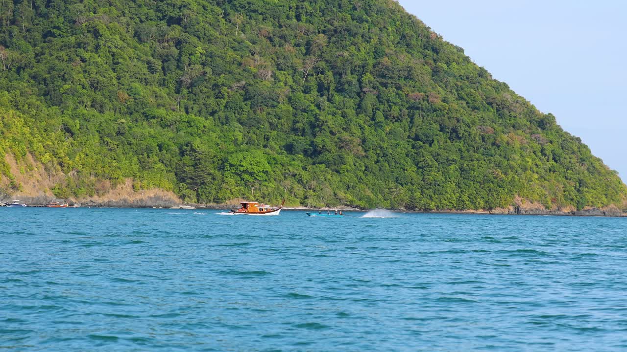 태국 푸켓 근처의 바다를 가로지르는 어선, 은 하늘 아래 푸른 언덕을 배경으로