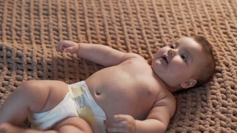 top view of little baby girl lying on knitted blanket and laughing