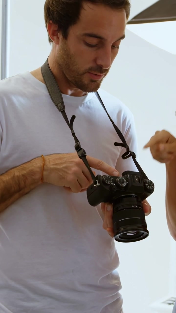 Video verticale: Professionista di studio che regola le manopole di una DSLR su indicazione della modella, con animazioni digitali intorno alle manopole.