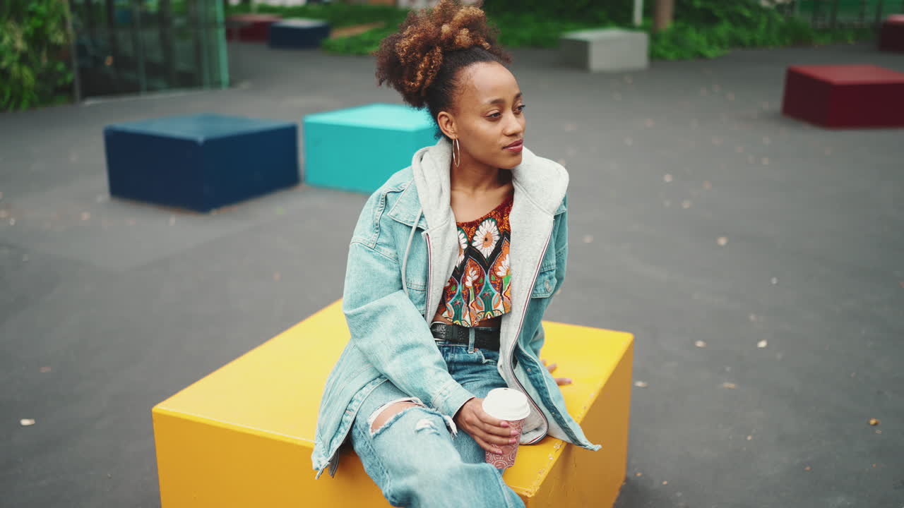 Woman sitting on a yellow cube in an urban environment