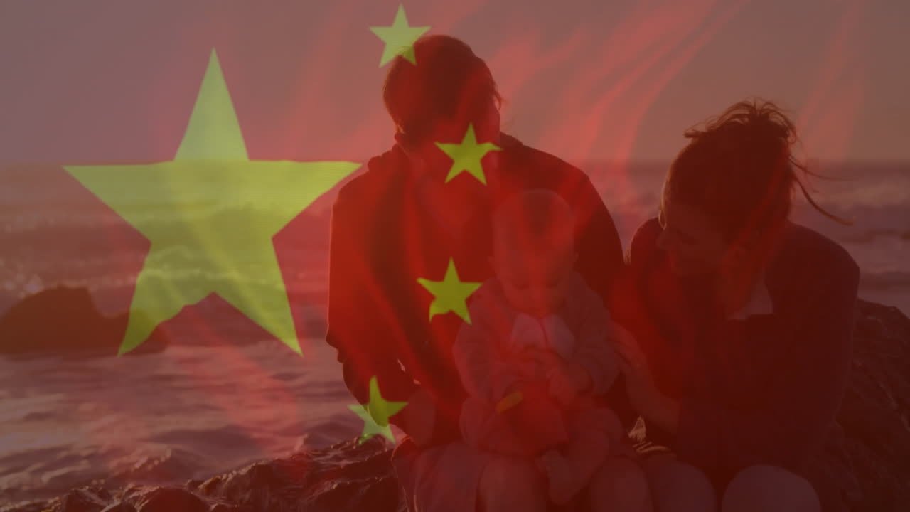 Sitting by ocean, family with Chinese flag animation overlay during sunset light