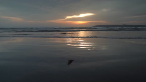 seascape view of ocean waves crashing on the sandy coastline, at sunset, on a cloudy evening