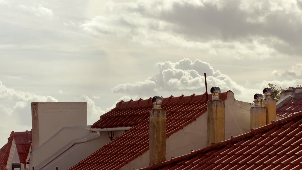 Tetti di tegole rosse con camini contro un cielo nuvoloso.
