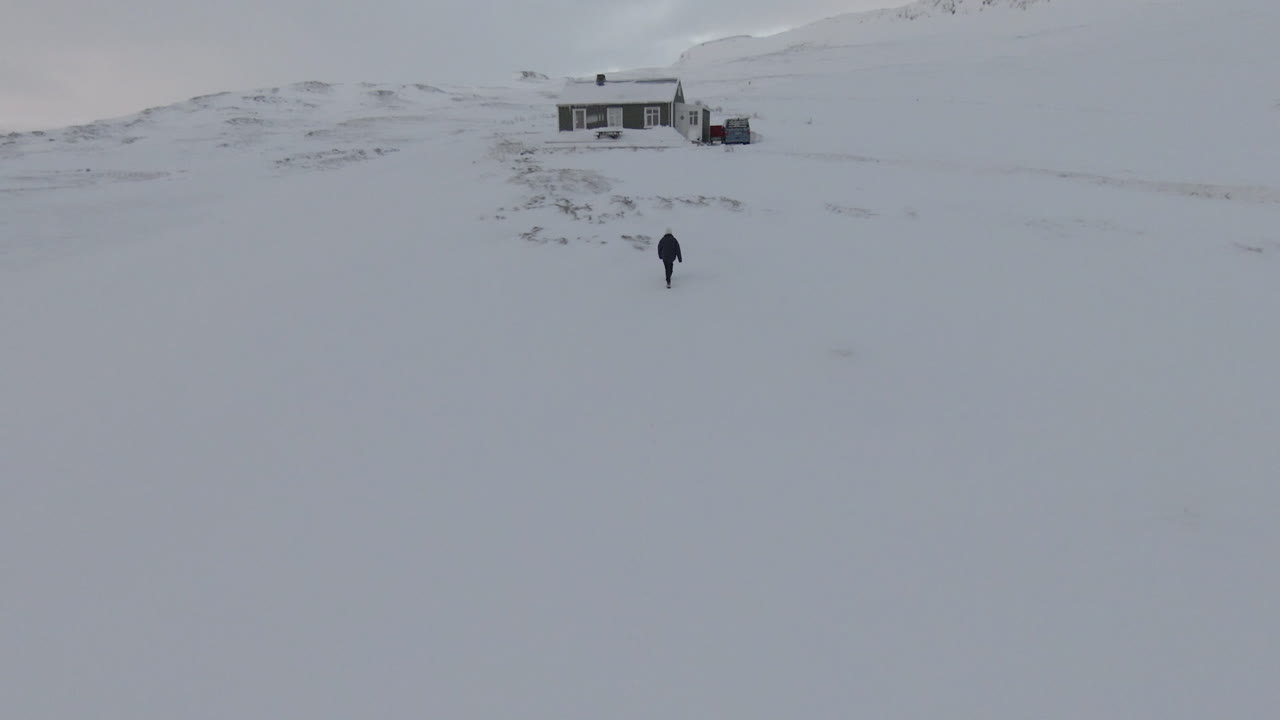 산 한가운데 눈 덮인 오두막을 향해 걸어가는 여자