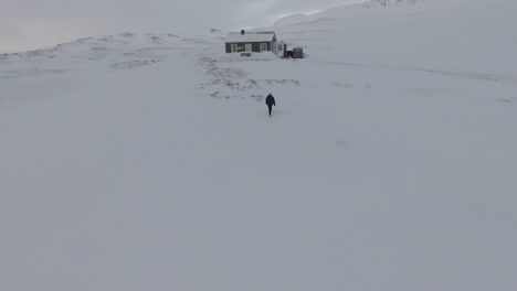 Woman-walking-towards-snowed-cabin-in-middle-of-mountains
