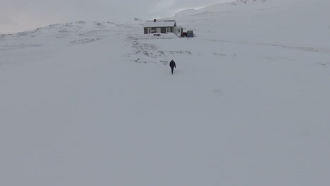 Frau-Zu-Fuß-In-Richtung-Verschneite-Hütte-Mitten-In-Den-Bergen