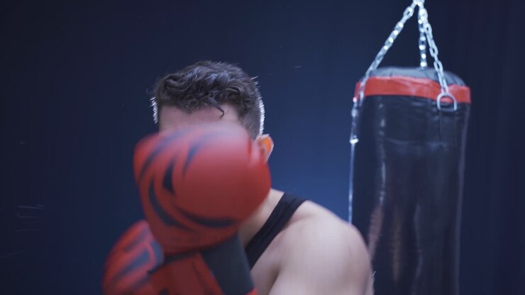 Pugile maschio aggressivo che fa pugilato professionalmente in una palestra buia.