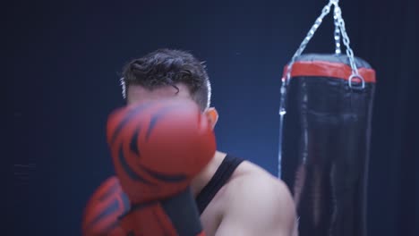 aggressive male boxer professionally boxing in a dark gym.