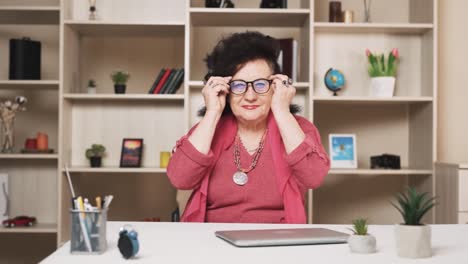 old woman puts on glasses and, opening a laptop, starts working and smiling at the camera