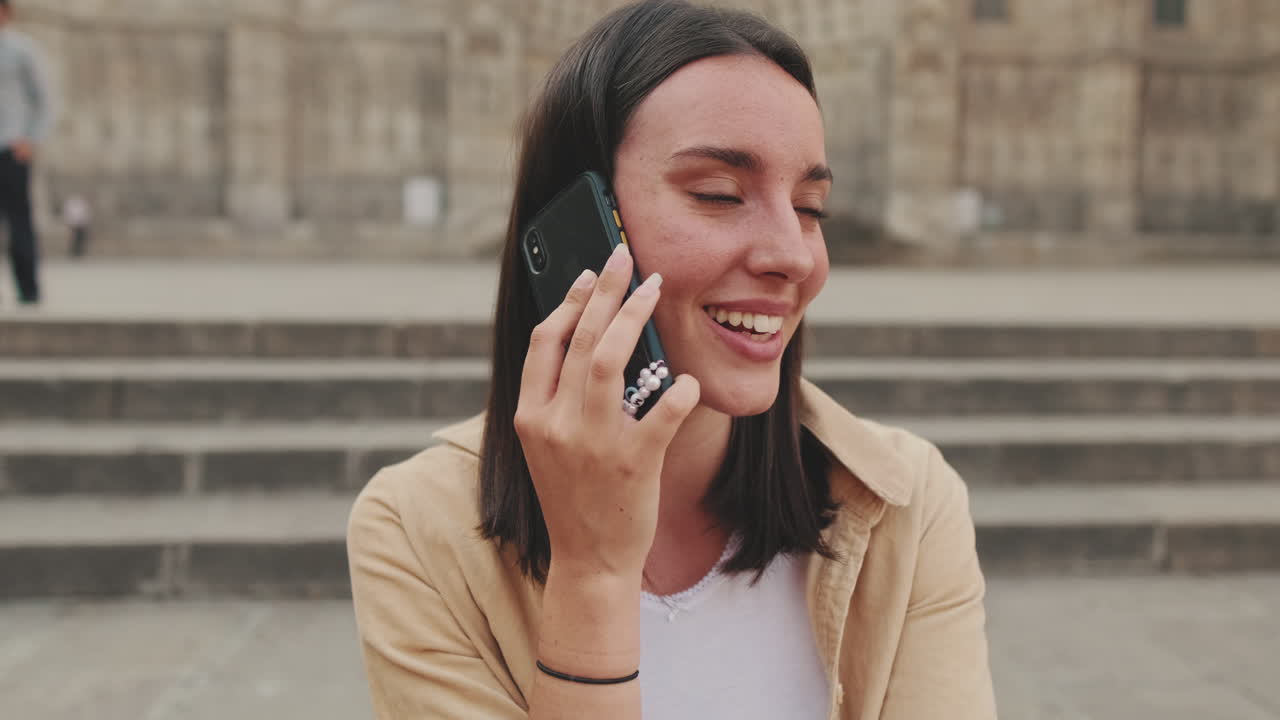 Giovane donna felice che parla e ride al telefono all'aperto.