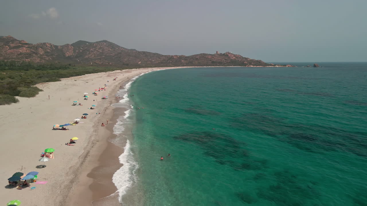무인 항공기는 이탈리아 사르데냐에서 화창한 날 동안 관광객이 휴식을 취하고 열대 해변을 즐기는 파도 위를 날고 있습니다.