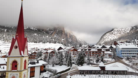 snowy mountain town with church steeple in selva di val gardena, italy