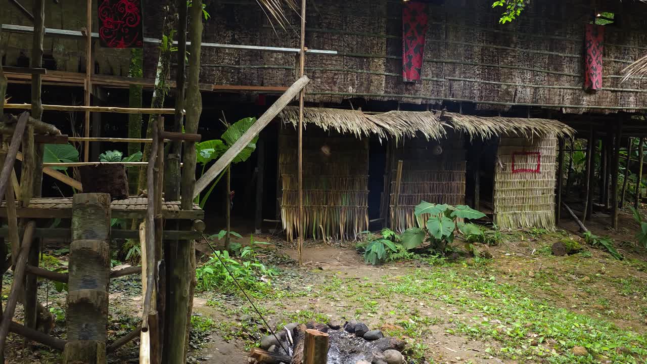 Detailed view of a traditional elevated house with thatched walls and roof, showing wooden steps and a fire pit, in Mari Mari village, Kota Kinabalu, Malaysia
