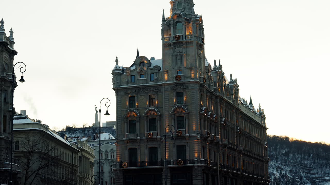 Edificio storico elegante nel centro di Budapest illuminato al crepuscolo durante l'inverno, che mostra l'architettura europea dettagliata e l'atmosfera urbana.